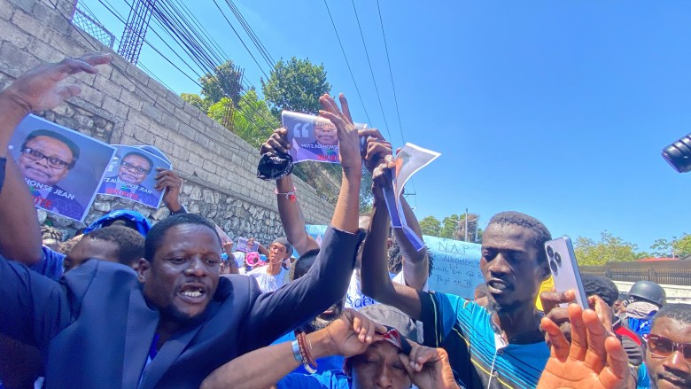 Protesters and supporters of Fritz Alphonse Jean as president of the transitional Presidential Council (CPT) gather in front of the Villa d’Acceuil in Port-au-Prince during the swear-in ceremony on March 7, 2025.  Phot by Arnold Junior Pierre for The Haitian Times. 
