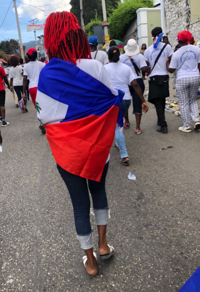 A protester wrapped in Haiti’s blue-and-red flag marched in Port-au-Prince on Saturday, Jan. 3, 2026, to call for peace amid insecurity and political instability. Photo by Juhakenson Blaise / The Haitian Times
